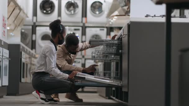 To personer med ansigtsmasker shopper i isenkræmmer ved pandemi af Covid-19, sorte ægtefæller vælger opvaskemaskine – Stock-video