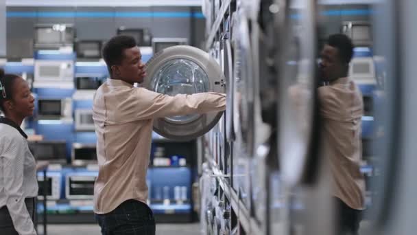 Afro-Amerikaanse echtgenoten zijn winkelen in huishoudelijke apparaten winkel, jonge man en vrouw zijn het bekijken van de wasmachine in hardware winkel — Stockvideo