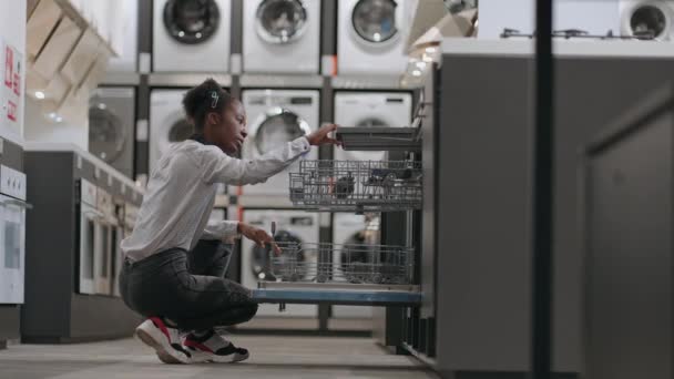 Jovem mulher negra está vendo novo modelo de máquina de lavar louça na loja eletrodomésticos, única senhora está comprando sozinho — Vídeo de Stock