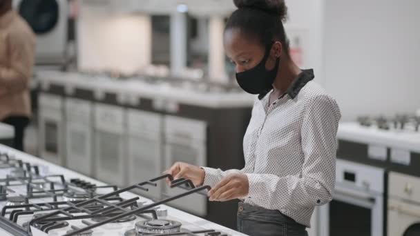 Visitantes están de compras en tiendas de electrodomésticos en el centro comercial, joven afroamericana mujer está viendo estufa de gas, la elección de nuevos equipos para la cocina — Vídeos de Stock