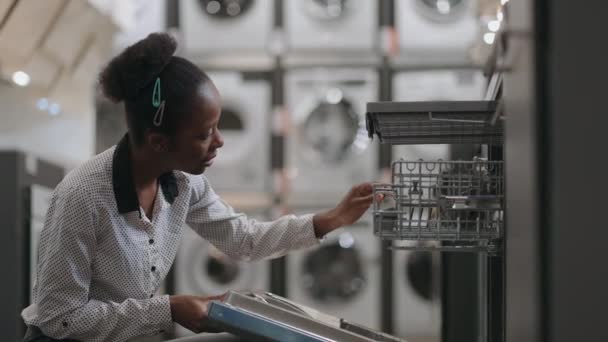 快乐的年轻黑人妇女正在家用电器商店里观看洗碗机，为厨房购买设备 — 图库视频影像