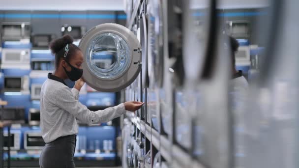 Joven mujer negra está eligiendo la lavadora en la tienda de electrodomésticos, comprador femenino está viendo la muestra de la exposición en la sala de comercio — Vídeo de stock