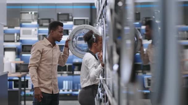 Vrolijk afro-Amerikaans paar is het kiezen van wasmachine in hardware winkel, man en vrouw zijn het bekijken van nieuwe modellen binnen — Stockvideo