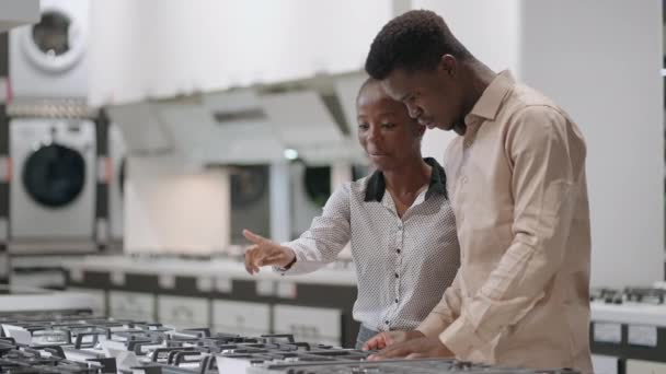 Lächelnde Afroamerikaner wählen Gasherd in Haushaltsgerätegeschäften in Einkaufszentrum, schwarze Männer und Frauen betrachten und diskutieren Ausstellungsproben — Stockvideo