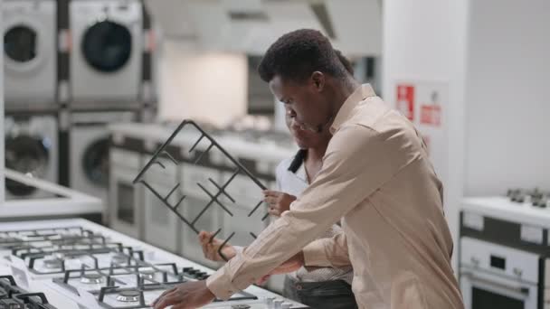 Joven afro-americano casado pareja está eligiendo estufa de gas en electrodomésticos tiendas en el centro comercial, hombre y mujer están viendo placa caliente — Vídeos de Stock