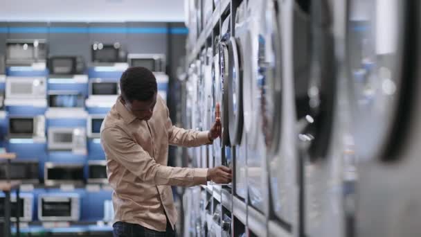 젊은 흑인 남성 이 가정용 가전제품 가게에서 세탁기를 선택하고 있습니다. — 비디오