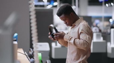 Afro-Amerikalı adam modern kulaklıkları ses ekipmanları mağazasında test ediyor. Alışveriş merkezinde orta boy erkek portresi.