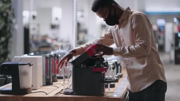 Afro-Amerikalı adam ev aletleri dükkanından otomatik kahve makinesini seçiyor. Maskeli genç adam alışveriş yapıyor. — Stok video