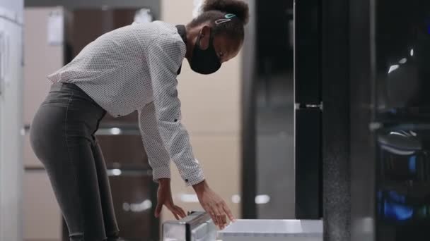 Mujer negra está viendo congelador de refrigerador en la tienda de electrodomésticos, ver la muestra de la exposición en el interior, retrato de comprador femenino en la sala de comercio — Vídeos de Stock