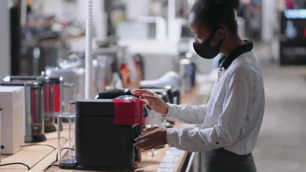 Jonge dame is winkelen in huis apparaat winkel, afro-Amerikaanse dame met gezichtsmasker is het kiezen van automatische koffiezetapparaat, het kopen van apparatuur voor keuken — Stockvideo