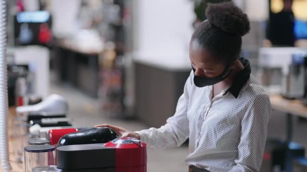 Jonge afro-Amerikaanse vrouw in keukenapparatuur winkel, jonge vrouwelijke shopper is het kiezen van automatische koffiezetapparaat voor thuis of op kantoor — Stockvideo