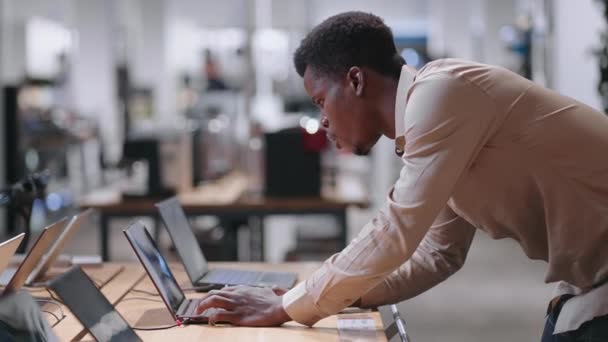 Hombre negro adulto está comprando portátil para el trabajo en la tienda de electrónica, probando el nuevo modelo en la sala de comercio — Vídeo de stock