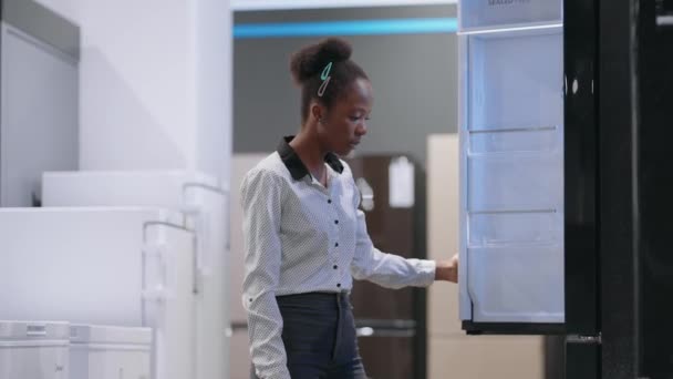 Afro-americká hospodyňka si vybírá chladničku v obchodě s domácími spotřebiči, prohlížení ukázky výstavy uvnitř, střední portrét — Stock video
