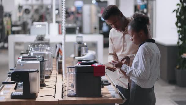 Černošky muž a žena si vybírají automatický kávovar v obchodě domácích spotřebičů, čtecí manuál moderního modelu — Stock video