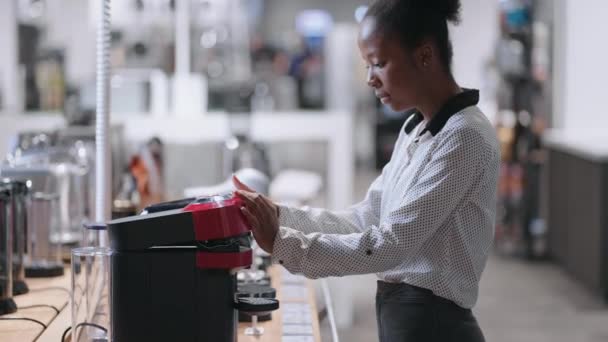 Νεαρή μαύρη γυναίκα σε κατάστημα συσκευών κουζίνας, γυναίκα αγοραστής επιλέγει αυτόματη καφετιέρα, πορτρέτο στην αίθουσα συναλλαγών — Αρχείο Βίντεο