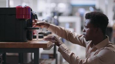 Genç Afro-Amerikalı adam, modern cihazlar almak için, mağazadan otomatik kahve makinesini seçiyor.