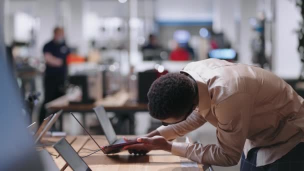 Genç Afro-Amerikalı adam elektronik mağazasında modern dizüstü bilgisayarı test ediyor. — Stok video