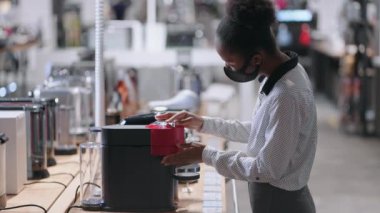 Genç siyah kadın ev aletleri dükkanından otomatik kahve makinesini seçiyor. Yüz maskeli Afro-Amerikan kadın.
