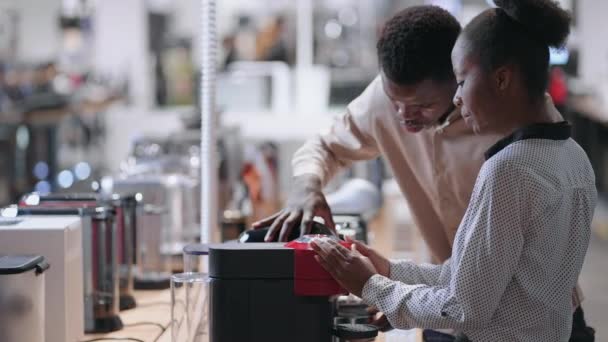 Afrikaans-Amerikaans echtpaar kiest koffiezetapparaat in huishoudelijke apparaten winkel, het vergelijken van verschillende monsters — Stockvideo