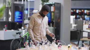 Yüzü maskeli erkek alışverişçi elektronik dükkanından alışveriş yapıyor. Gösteri vitrininde ukala bakışları izliyor.