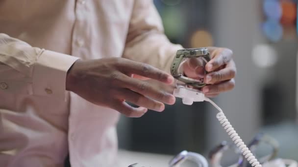 Surtido de relojes inteligentes modernos en la tienda de electrónica, hombre negro está tomando diferentes modelos y visualización — Vídeo de stock