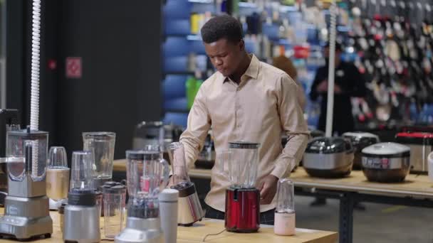 Афроамериканец выбирает блендер в кухонном магазине, одинокий мужчина покупает оборудование для кухни в новой квартире — стоковое видео