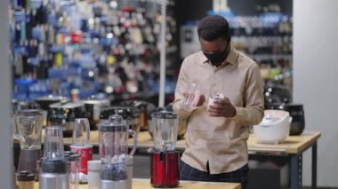 Genç siyahi adam mutfak gereçleri bölümünde mini blender izliyor, yemek yapmak için ekipman seçiyor.