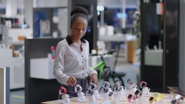 Mladá afro-americká nakupující žena si vybere chytráka v obchodě s digitálním vybavením, prohlíží si modely na předváděcím vitríně — Stock video