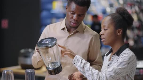 黒人男性と女性は家庭用電化製品店で台所用の機器を購入しブレンダーの展示サンプルについて話し合い — ストック動画