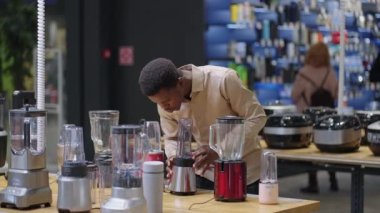 Genç adam ev aletleri mağazasından alışveriş yapıyor, mutfak için blender seçiyor, erkek alışverişçinin orta boy portresi.