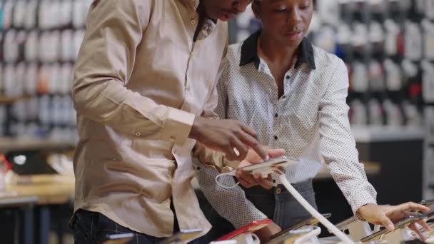 Afro-amerykański mężczyzna i kobieta robią zakupy w sklepie ze sprzętem cyfrowym, klienci omawiają różne modele smartfonów — Wideo stockowe