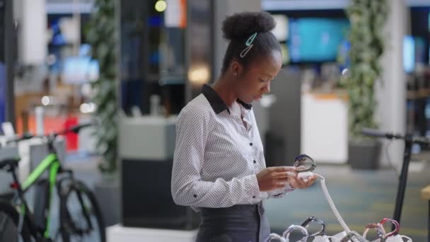 Mladá moderní žena nakupuje v obchodě s digitálním vybavením, prohlíží si nový model Smartwatch, odebere vzorek z předváděcího vitríny — Stock video