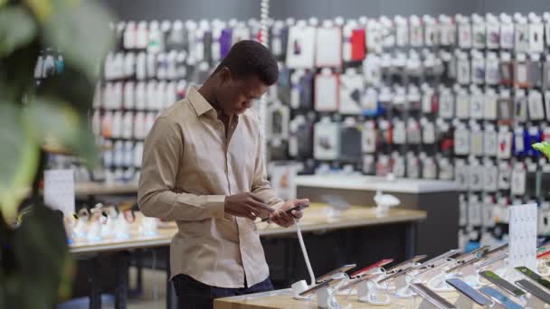 Zwarte man is winkelen in de mobiele telefoon winkel, het testen van moderne smartphone in de handelshal van de grote winkel — Stockvideo