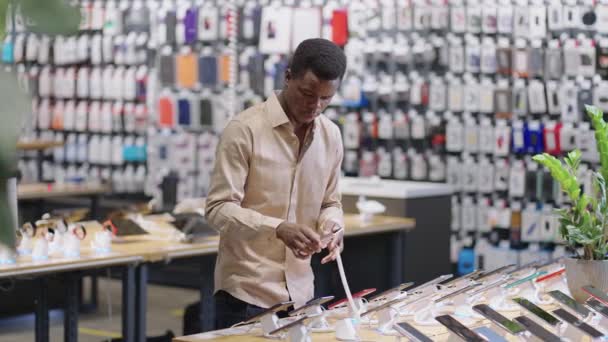 Afro-amerikanska manliga shoppare visar nya modeller av smartphones i demonstration visa upp handel hall av stora digitala utrustning butik — Stockvideo