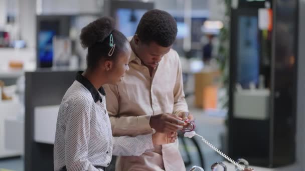 Muž a žena nakupují v obchodě s digitálním vybavením, černý pár si prohlíží nový model Smartwatch, odebírá vzorek z ukázkové vitríny — Stock video