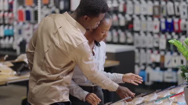 Jovens afro-americanos estão comprando em loja de equipamentos digitais, homem e mulher estão escolhendo smartphone — Vídeo de Stock
