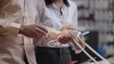 Erkek ve kadın dijital ekipman mağazasında akıllı telefon modellerini karşılaştırıyor, sergi örneklerinin arayüzünü kontrol ediyorlar