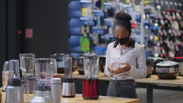 Afroamerikanische Shopperin mit Gesichtsmaske wählt Mixer im Geschäft, sieht sich Ausstellungsmuster auf Vitrine an — Stockvideo