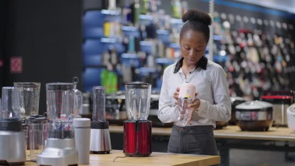 Schwarze Hausfrau wählt Mixer für Smoothies im Geschäft, sieht Ausstellung Probe, afroamerikanische Frau ist im Geschäft einkaufen — Stockvideo