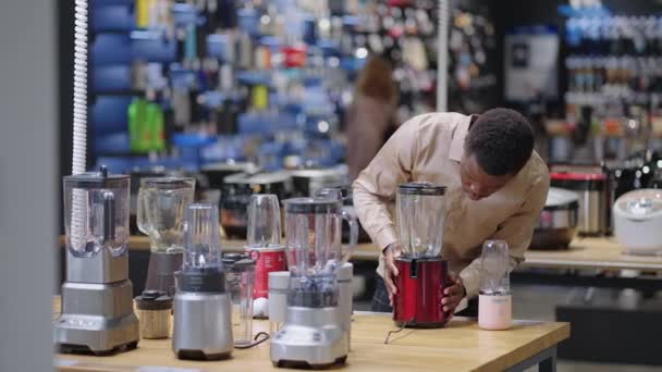 Afroamerikanischer Mann wählt Mixer im Geschäft für Küchengeräte, kauft Geräte zum Kochen, zeigt Proben in der Vitrine — Stockvideo