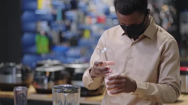 Shopping in kitchen appliances store during pandemic of covid-19, black man with face mask is choosing blender in kitchen equipment department — Stock Video