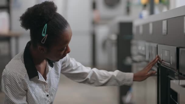 Fekete nő választja elektromos sütő háztartási gépek bolt, háziasszony összehasonlítja kiállítási minták kereskedelmi csarnok — Stock videók