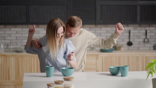 Funny active young couple in love dancing in kitchen. Cheery wife in dress hold her lively husband hand, cheerful family listen music enjoy carefree weekend at new modern warm home. Fun, hobby concept — Stock Video