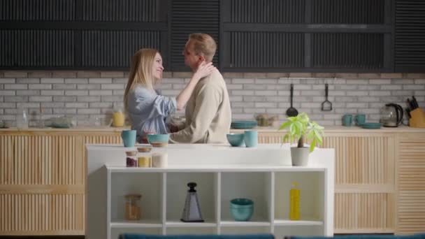 A young couple man and woman in the morning dance together to the music. A cheerful couple husband and wife flirt and dance in the morning in the kitchen — Stock Video