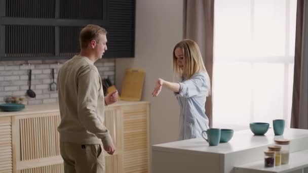 Funny active young couple in love dancing in kitchen. Cheery wife in dress hold her lively husband hand, cheerful family listen music enjoy carefree weekend at new modern warm home. Fun, hobby concept — Stock Video