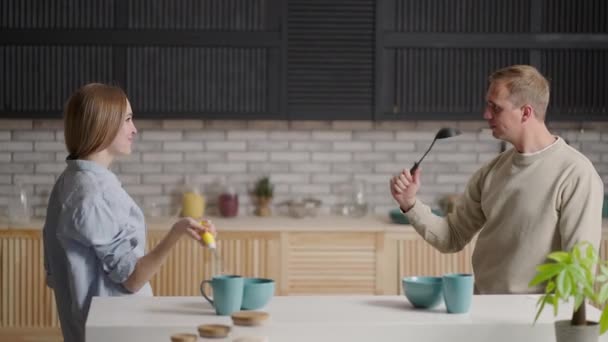 Jovem casal alegre se divertir dançando e cantando enquanto definir a mesa para o café da manhã na cozinha em casa — Vídeo de Stock