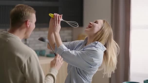 Jóvenes feliz familia activa pareja bailando riendo juntos preparando la comida en casa, sin preocupaciones alegre marido y esposa divirtiéndose cocinar comida romántica saludable cena escuchar música en la cocina moderna — Vídeo de stock