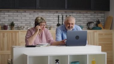 Emekliler sigorta ve mali danışmana danışmanlık yapıyor. Ev mutfağında oturuyorlar. Evde yaşlı bir çiftin orta boy portresi var.