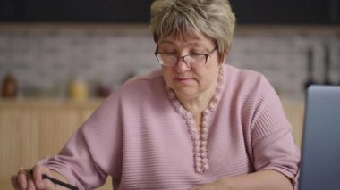 Yaşlı kadın evden uzaktan çalışıyor, hesap makinesiyle sayıyor ve laptopla dolduruyor, yaşlı kadının portresi.