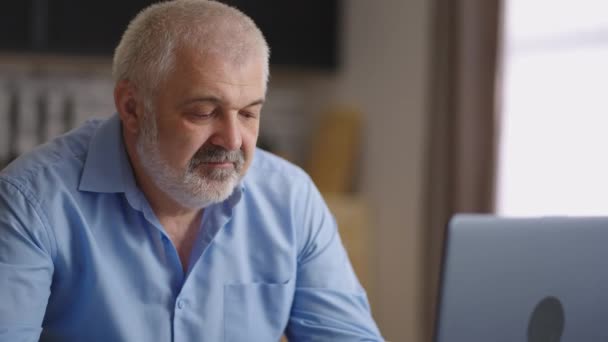 Vecchio sta lavorando da casa, navigare in internet tramite computer portatile in appartamento, lavoro lontano durante la pandemia di coronavirus — Video Stock